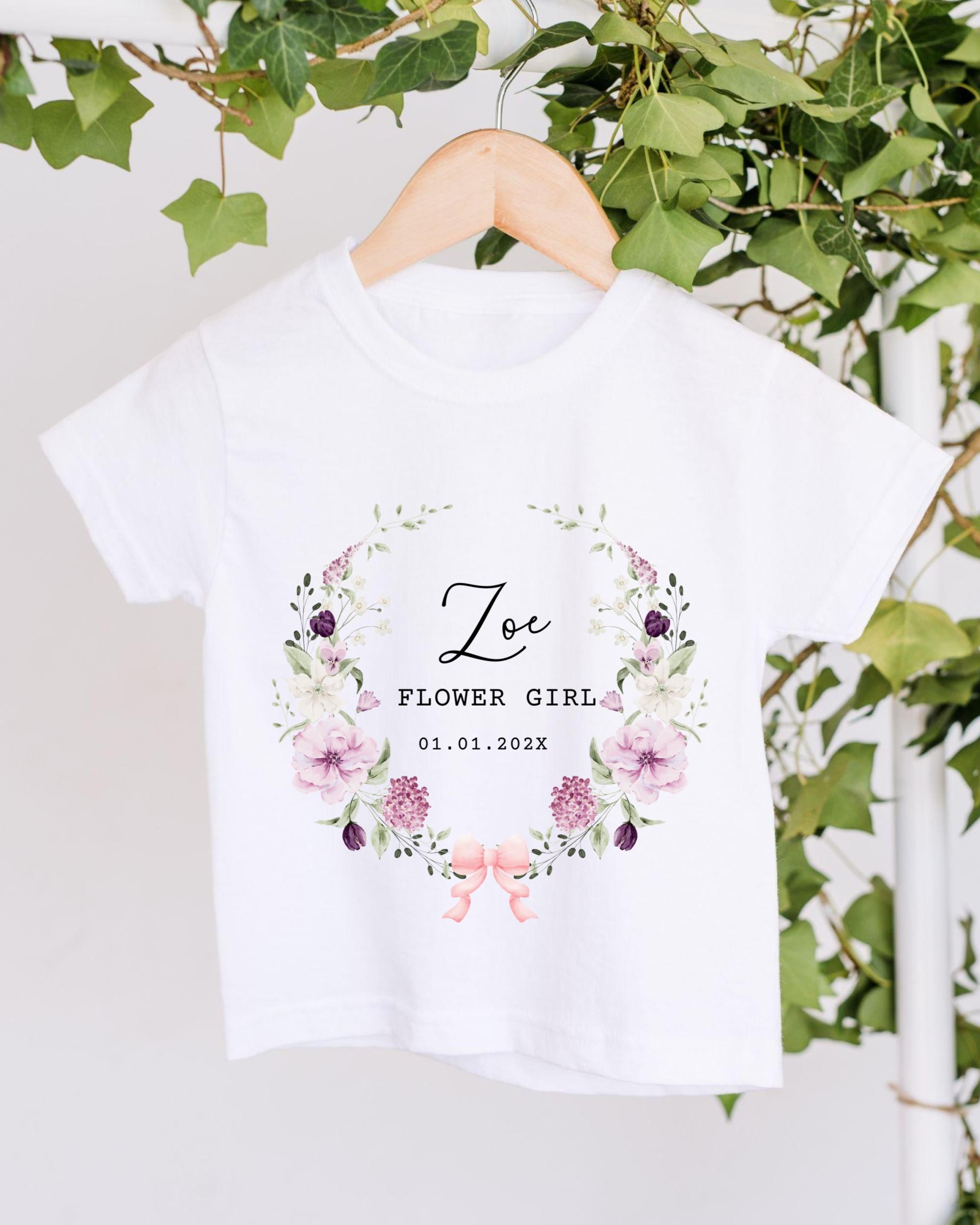 A white t-shirt with a floral design and text printed on it, hanging on a wooden hanger.