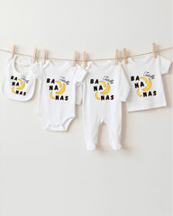A collection of white baby clothes, including onesies and bibs, with the word "BAANA" printed on them. The clothes are hanging on a clothesline, with the clothespins holding them in place.