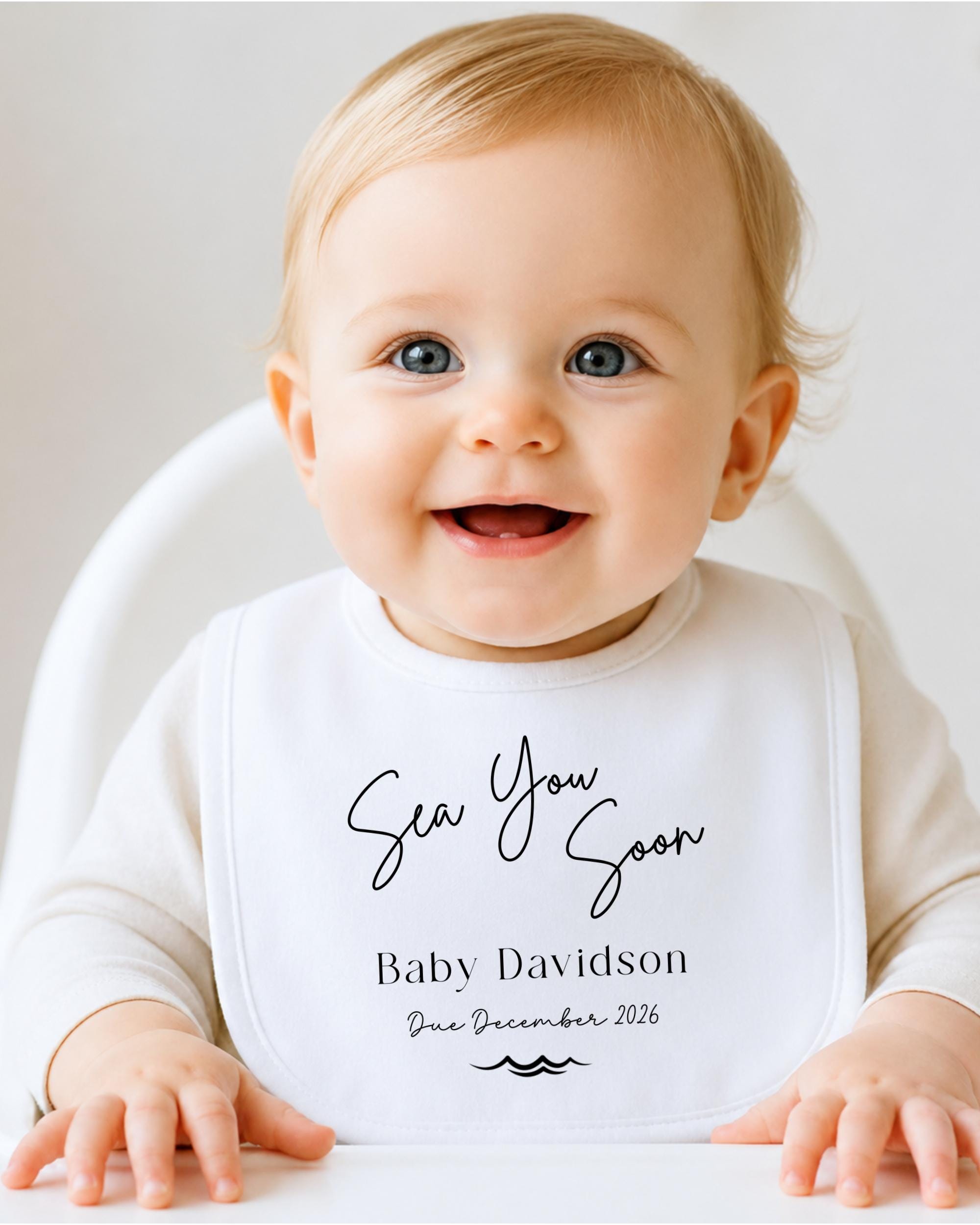 A smiling baby wearing a white bib with the text "Sea You Soon Baby Davidson Due December 2026" printed on it.