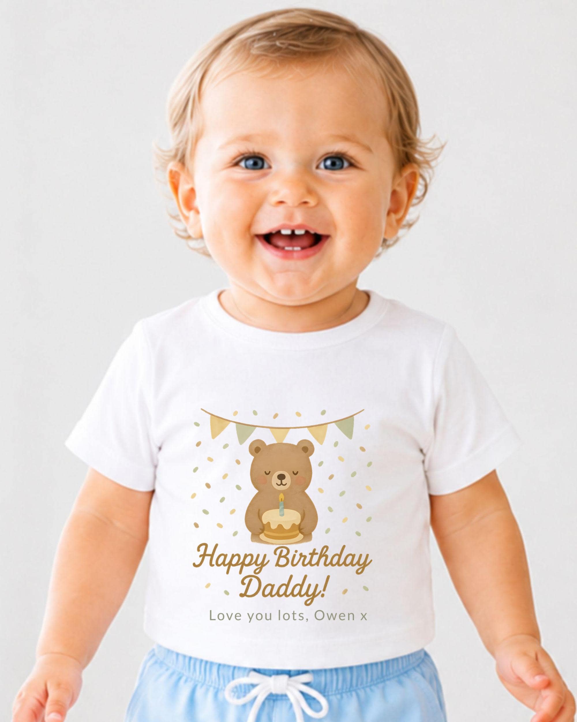 A smiling baby boy wearing a white t-shirt with a birthday message and a bear graphic.
