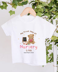 A white t-shirt with a teddy bear and a chalkboard, along with the text "My First Day at Nursery Lisa" and "September 2020".