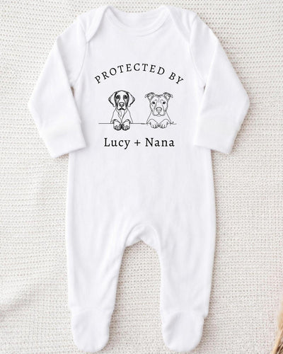 A white bodysuit with a graphic design featuring two cartoon dogs and the text "PROTECTED BY Lucy + Nana" printed on it.
