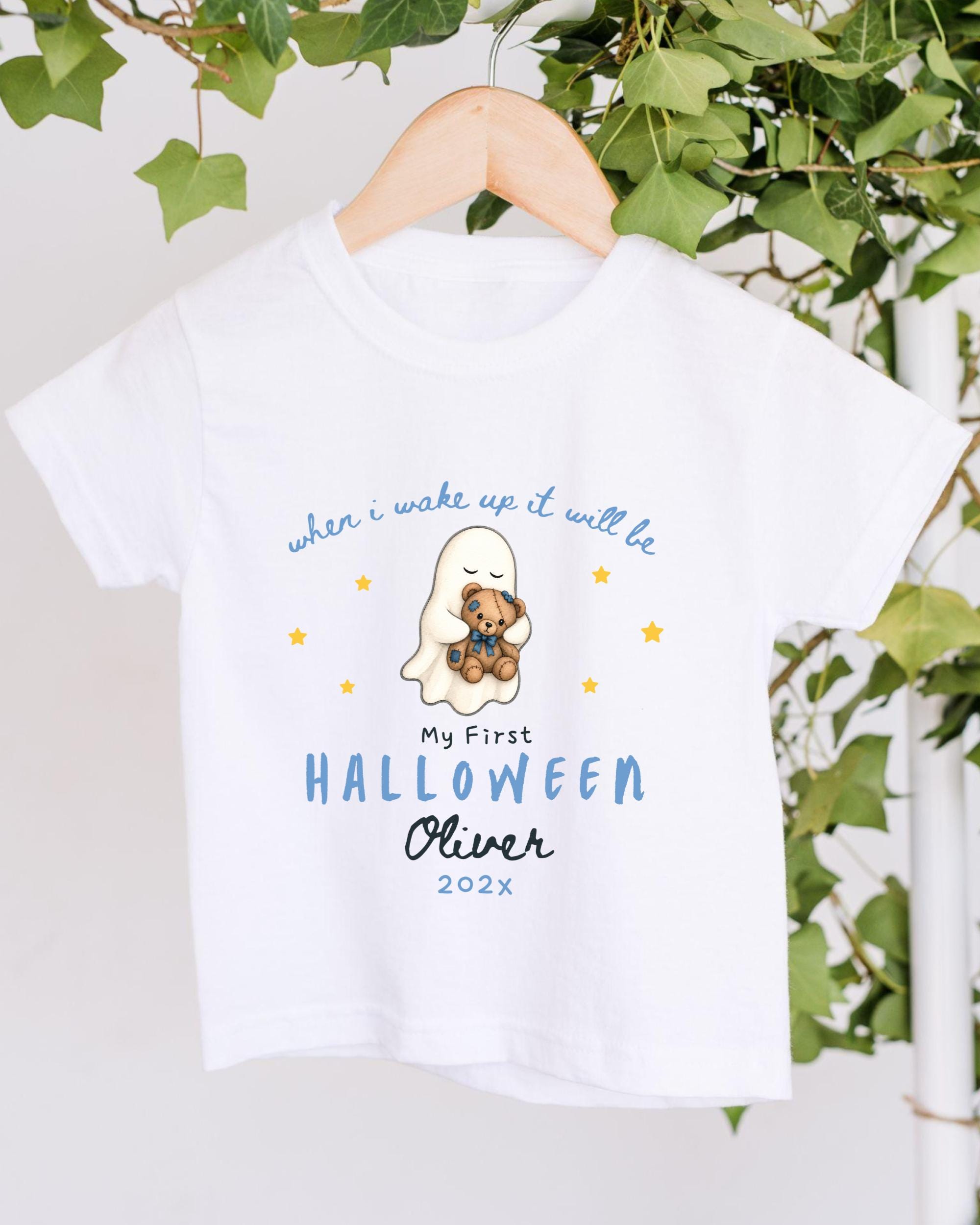 A white t-shirt with a graphic design featuring a ghost and a teddy bear, along with text that says "when I wake up it will be my first Halloween Oliver 2020x".