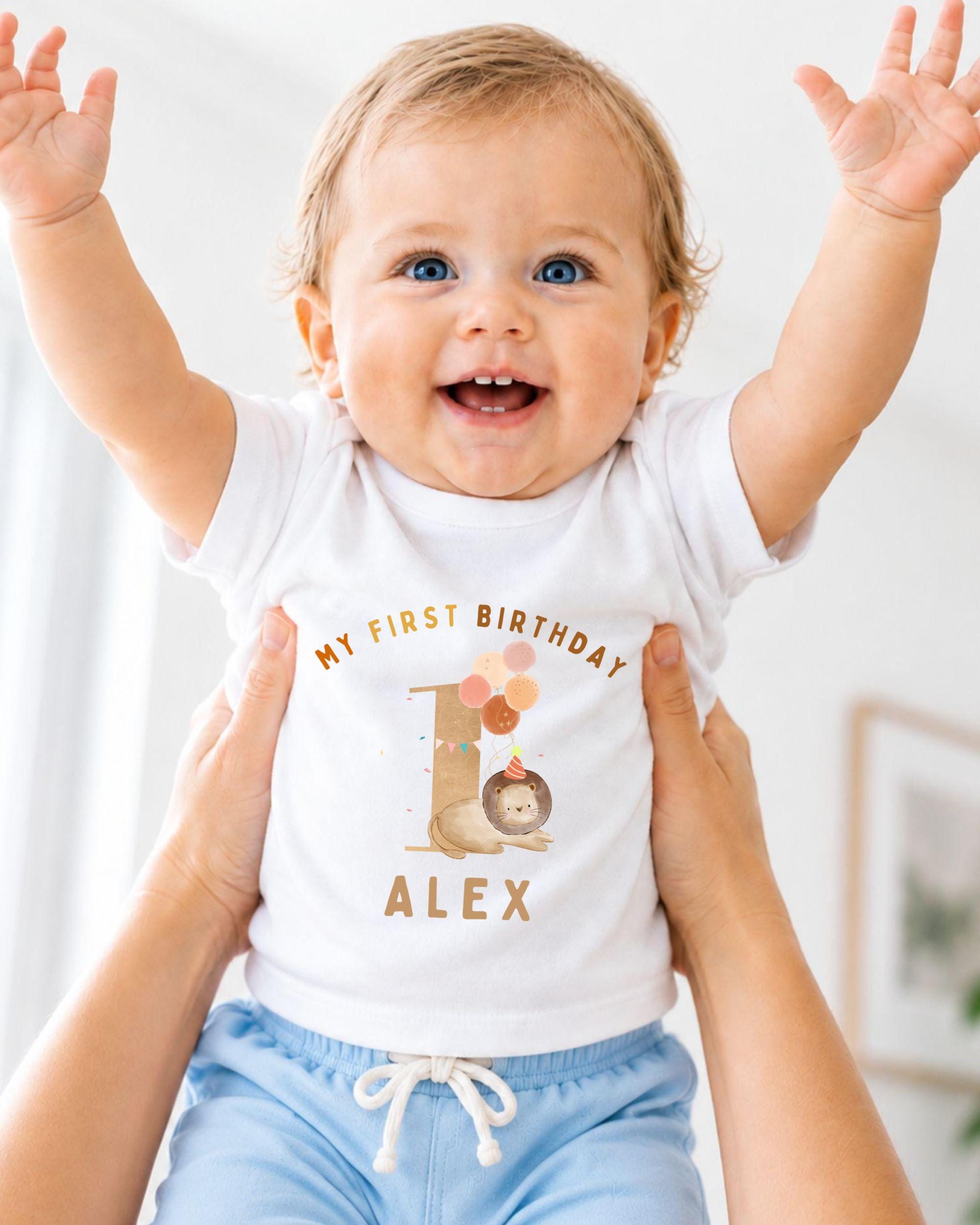 A smiling baby wearing a white t-shirt with a personalized birthday message and a cartoon character.