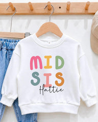 A white sweatshirt with colorful text printed on it, hanging on a wooden hanger.