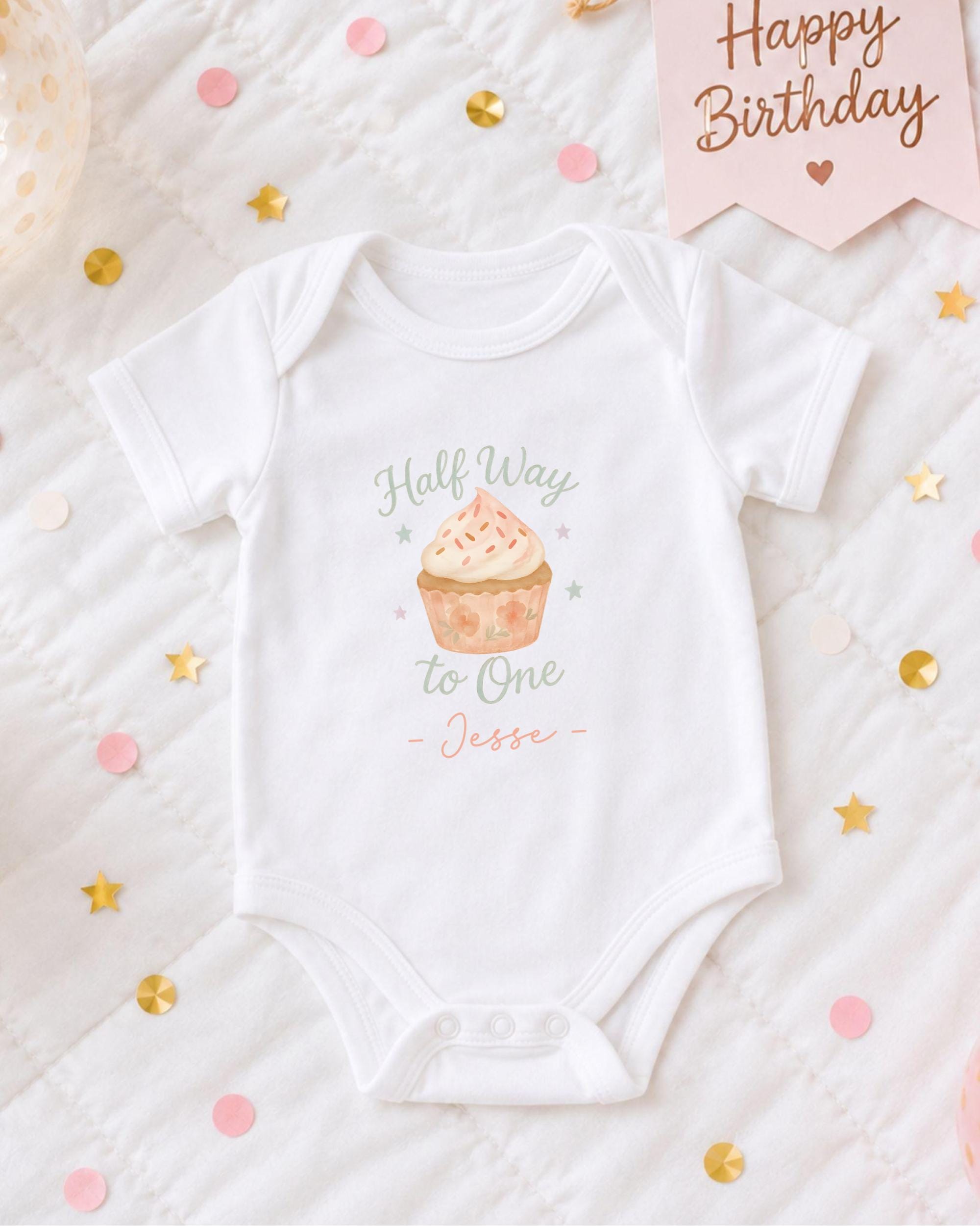 A white onesie with a cupcake design and the text "Half Way to One - Jesse" printed on it, along with confetti and a birthday card.