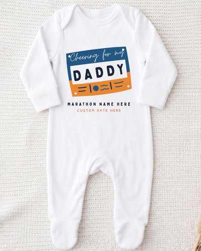 A white onesie with a graphic design on it, featuring the text "Cheering for my DADDY" and "MARCHON NAME HERE" along with a custom name.