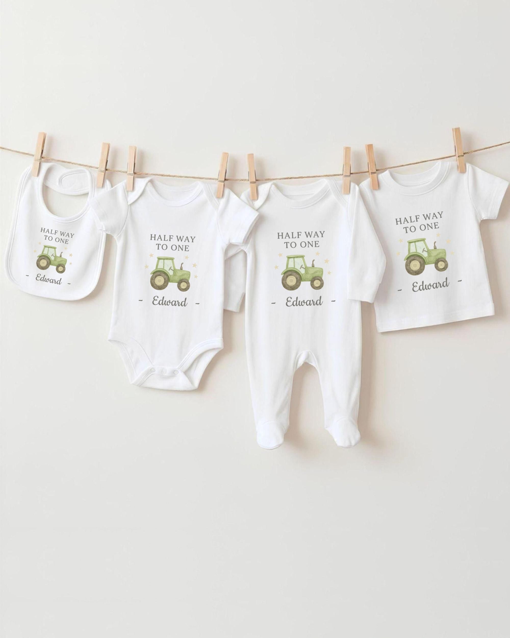 A collection of white baby clothes, including onesies and bibs, with a tractor printed on them, hanging on a clothesline.