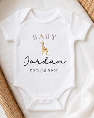 A white baby onesie with the text "BABY Jordan Coming Soon" printed on it, along with a small giraffe illustration.
