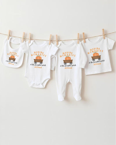 A row of four white baby clothes with a pumpkin patch design, hanging on a clothesline.