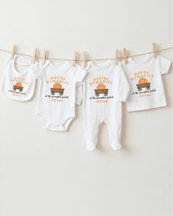 A row of four white baby clothes with a pumpkin patch design, hanging on a clothesline.