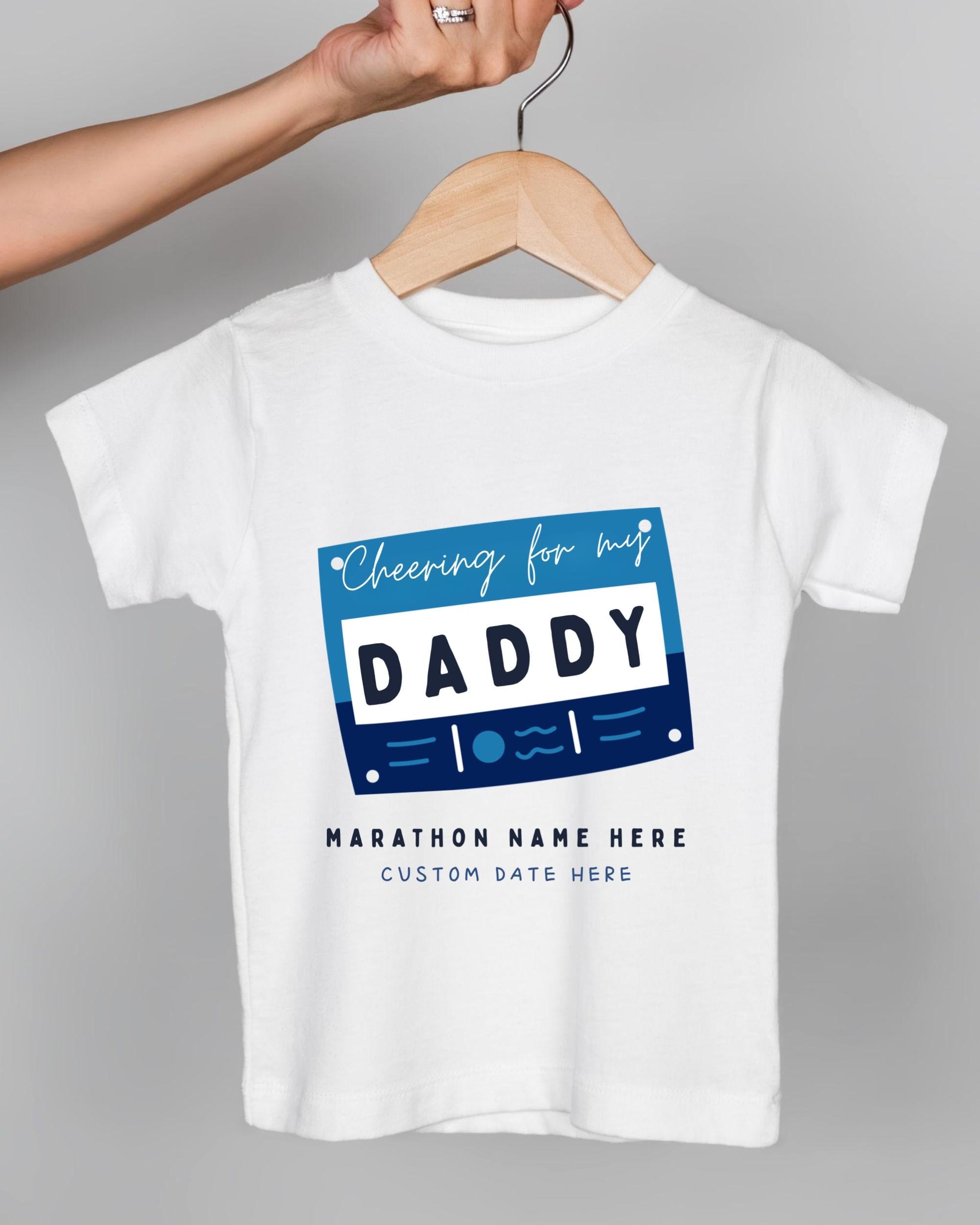 A white t-shirt with a graphic design featuring a blue and white "DADDY" text box, along with the text "Cheering for my DADDY" and "Marathon Name Here Custom Date Here".