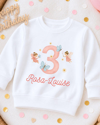 A white sweatshirt with a pink number 3 and a fairy design, along with the text "Rosa-Louise" printed on it.