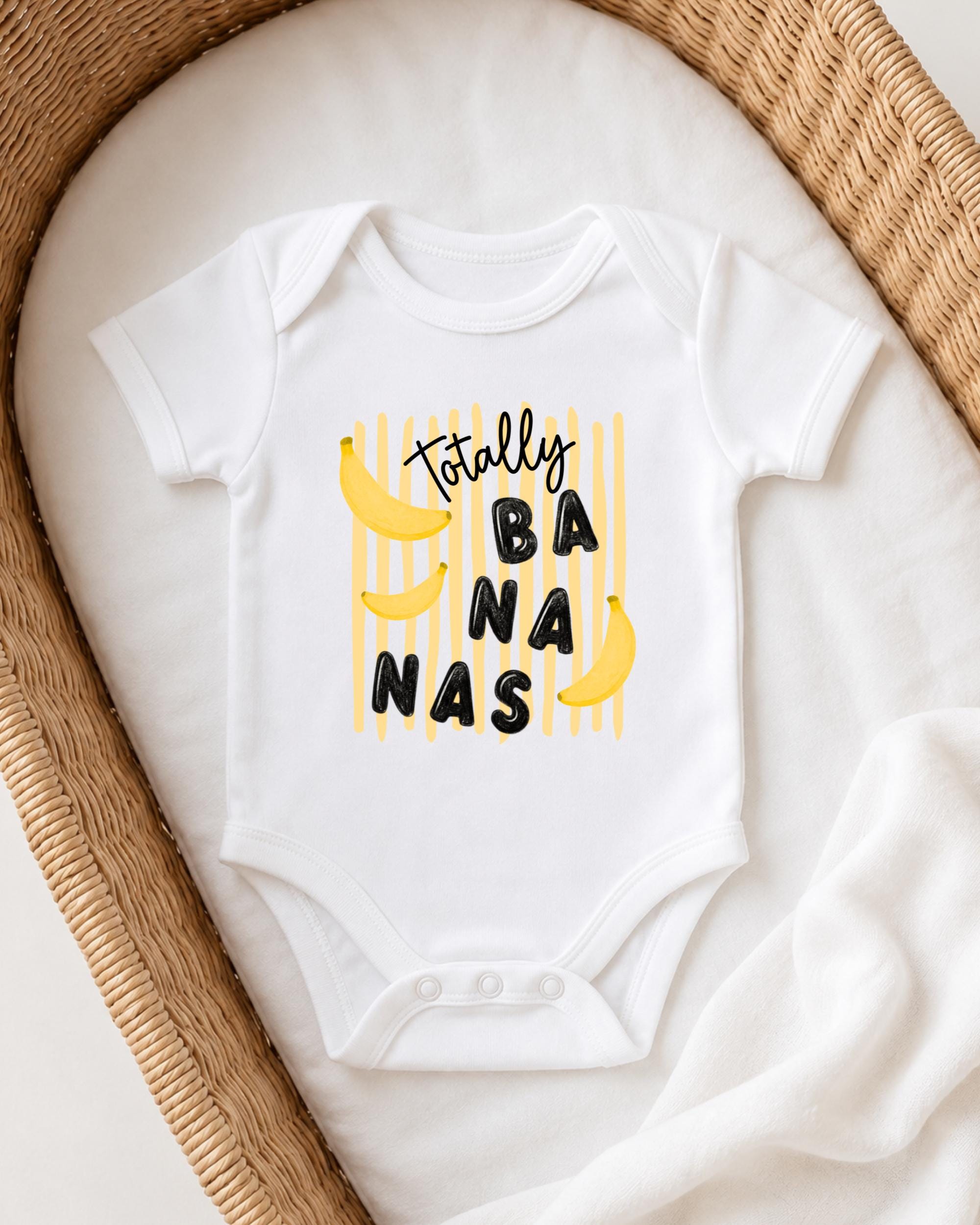A white onesie with a playful banana graphic and the text "Totally BANANA" printed on it, laid out on a white blanket.