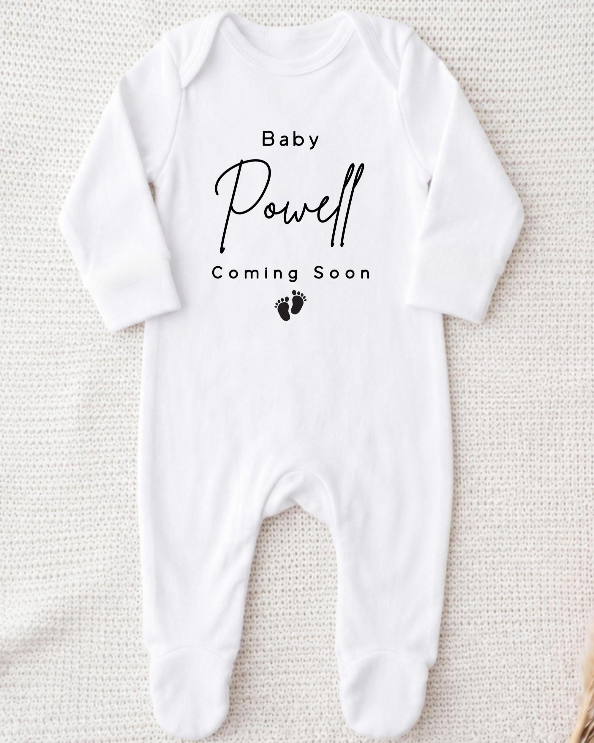 A white onesie with the text "Baby Powell Coming Soon" printed on it.