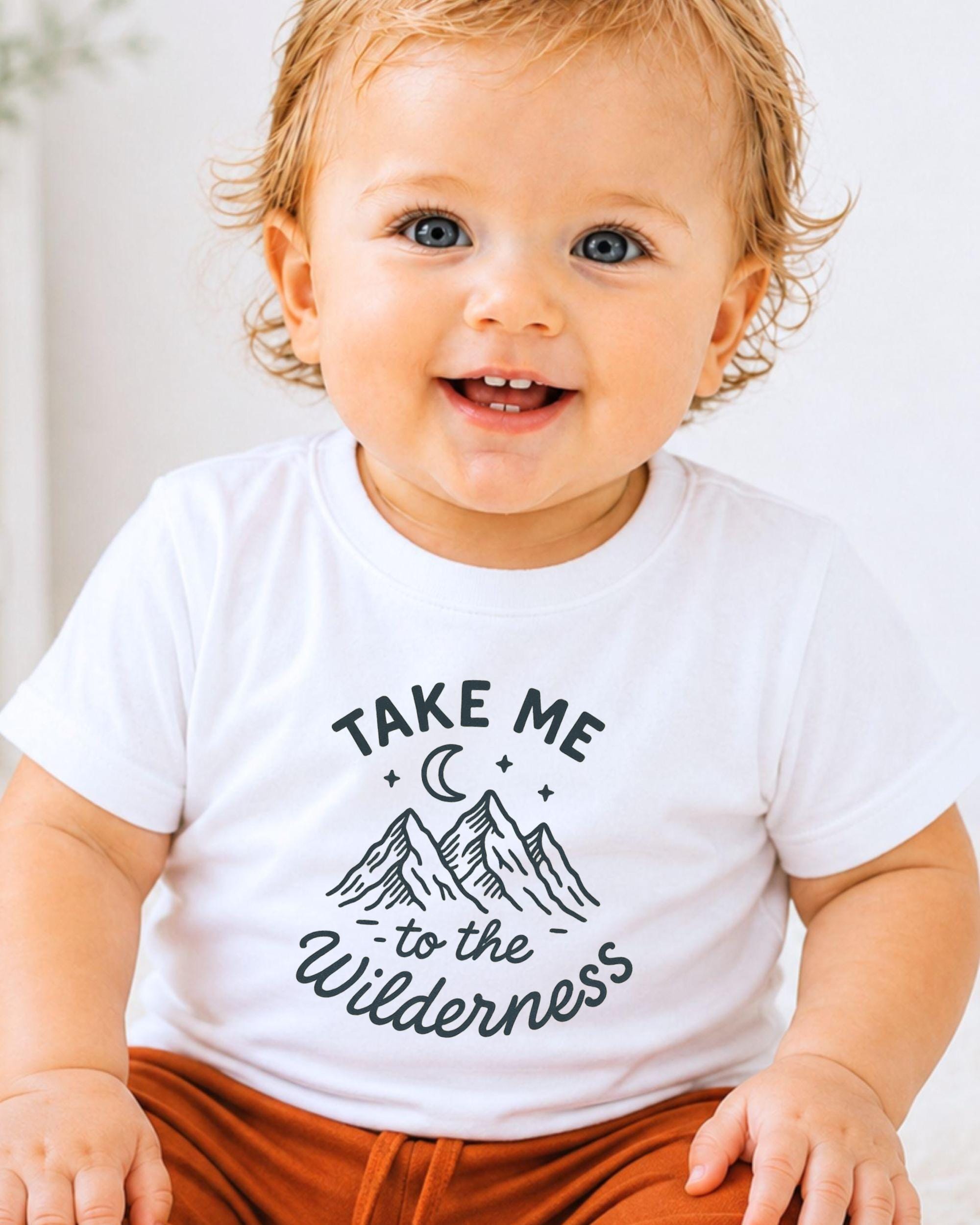 A smiling baby wearing a white t-shirt with a graphic design and text printed on it.
