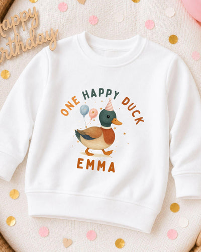 A white sweatshirt with a cartoon duck and the text "One Happy Duck Emma" printed on it, surrounded by confetti.