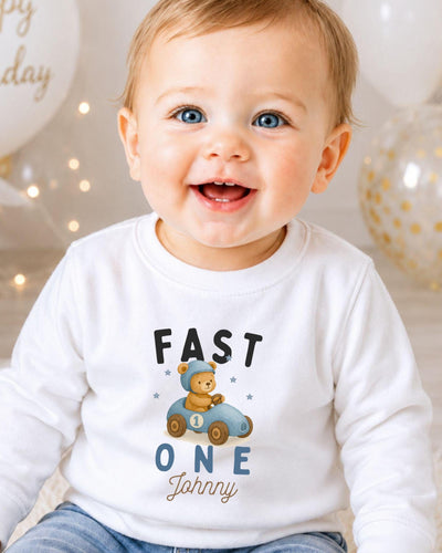 A smiling baby boy wearing a white shirt with a teddy bear and the text "FAST ONE Johnny" printed on it.