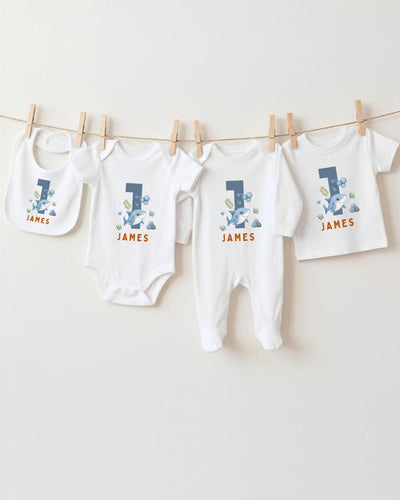 A collection of white baby clothes, including bodysuits and pants, with the name "James" printed on them. The clothes are hanging on a clothesline, with the first two items being bibs and the third one being a regular-sized shirt.