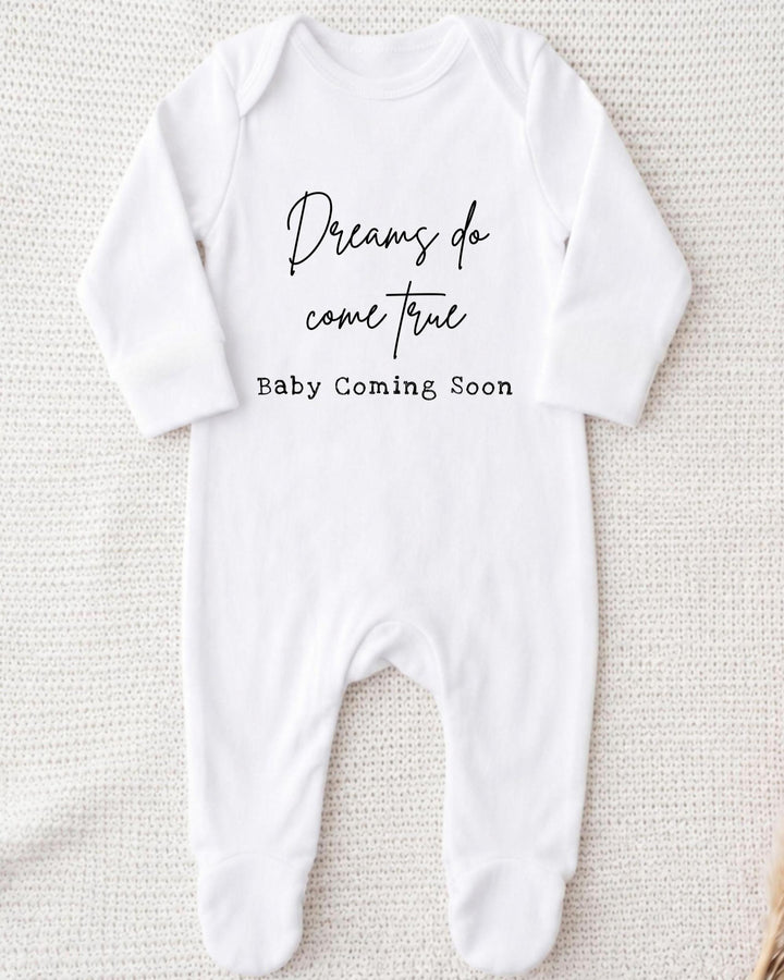 A white bodysuit with the text "Dreams do come true Baby Coming Soon" printed on it.