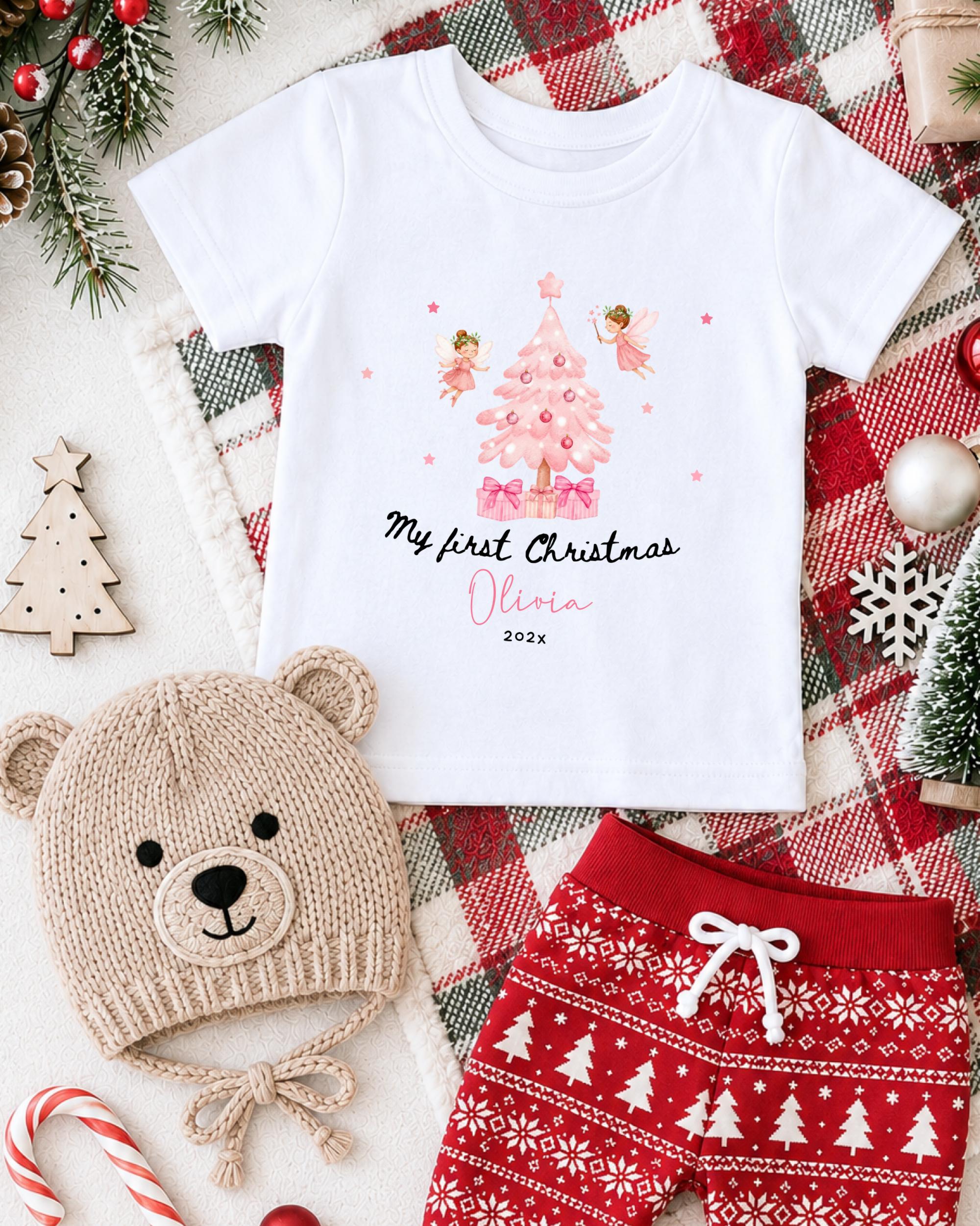 A white t-shirt with a Christmas tree design and the text "My first Christmas Olivia" printed on it, along with a teddy bear hat and red patterned shorts, all set against a backdrop of Christmas decorations and ornaments.