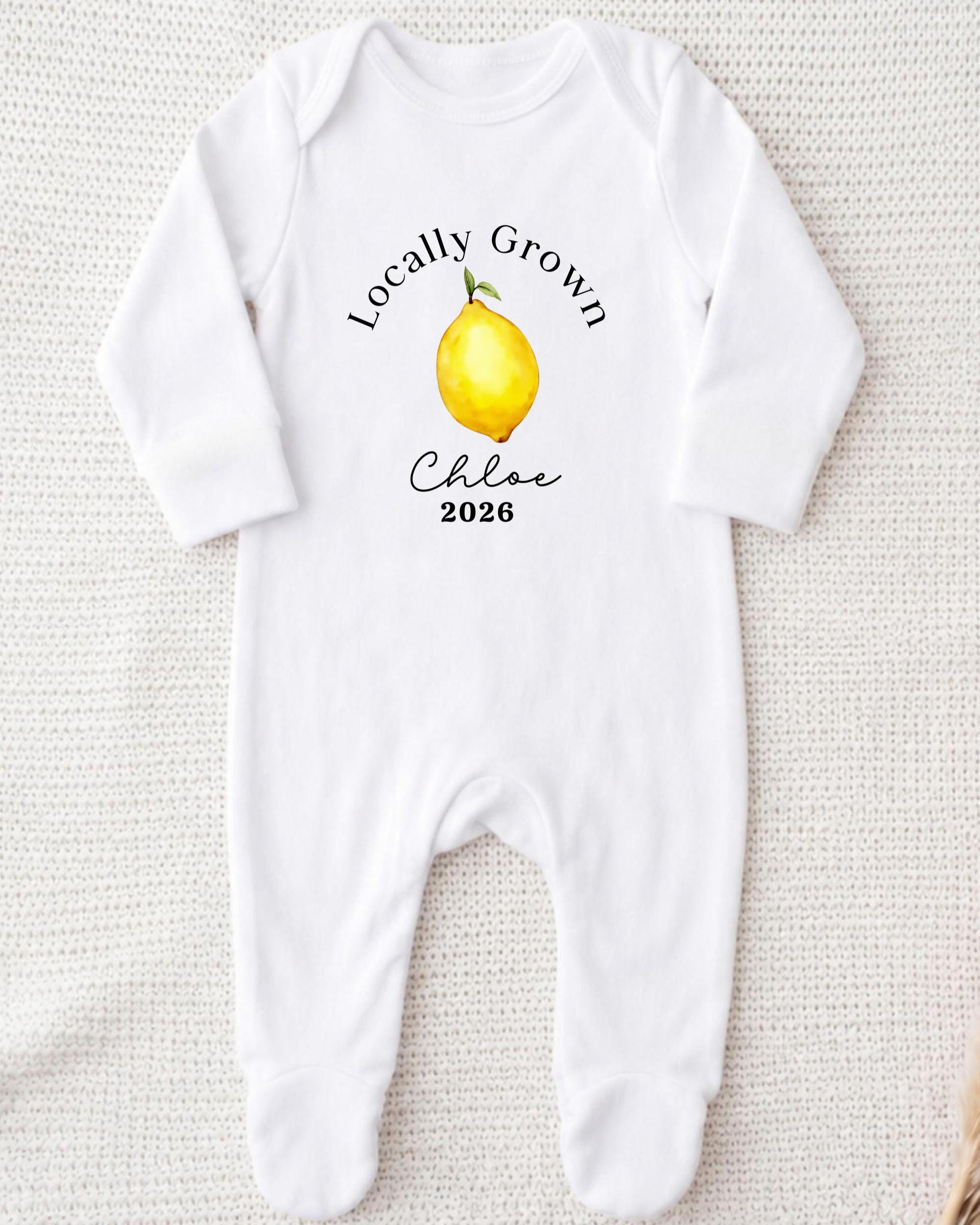 A white onesie with a printed design of a lemon and the text "Locally Grown Chloe 2026" printed on it.