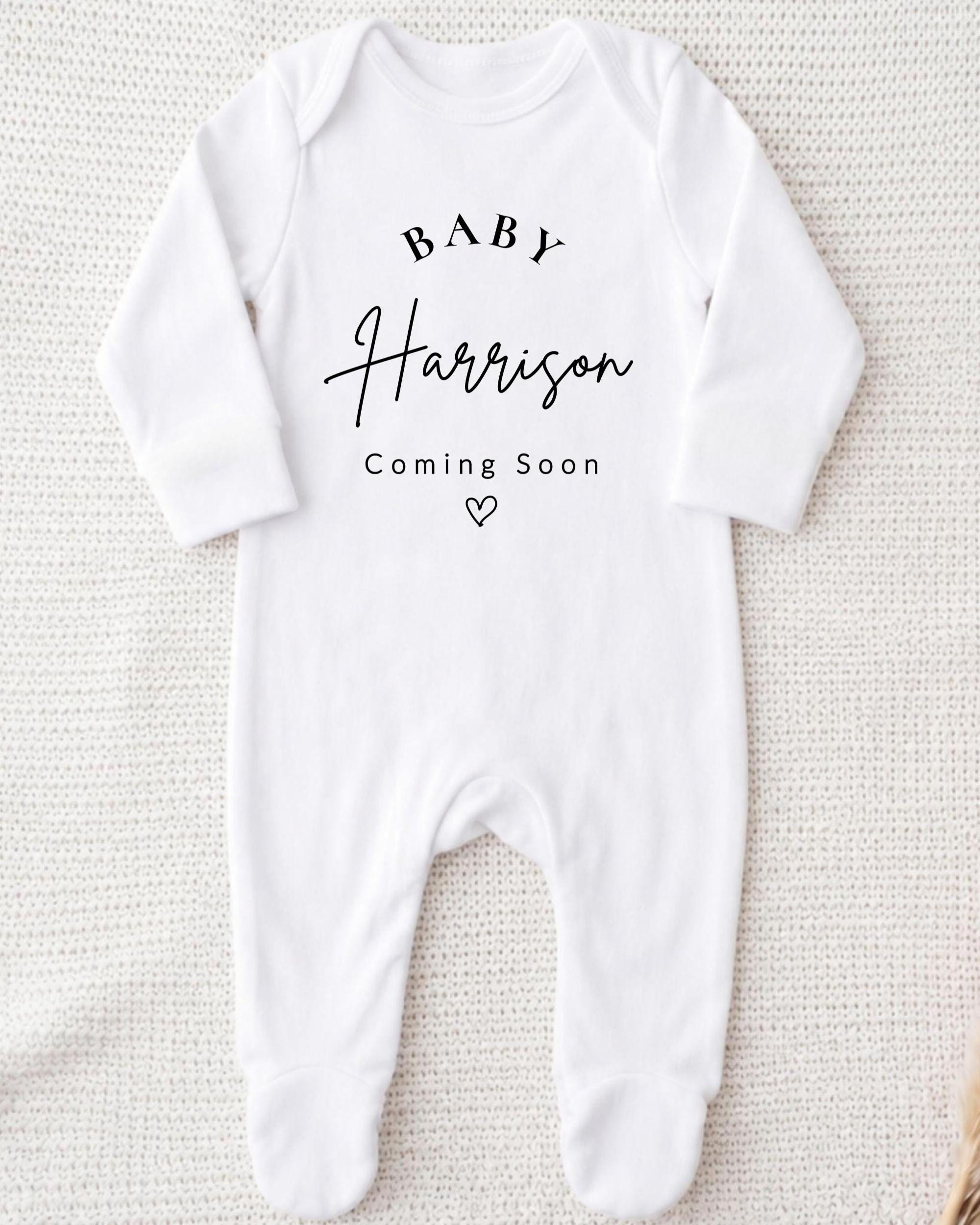 A white onesie with the text "BABY Harrison Coming Soon" printed on it.