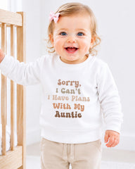A smiling baby girl wearing a white sweater with text on it.