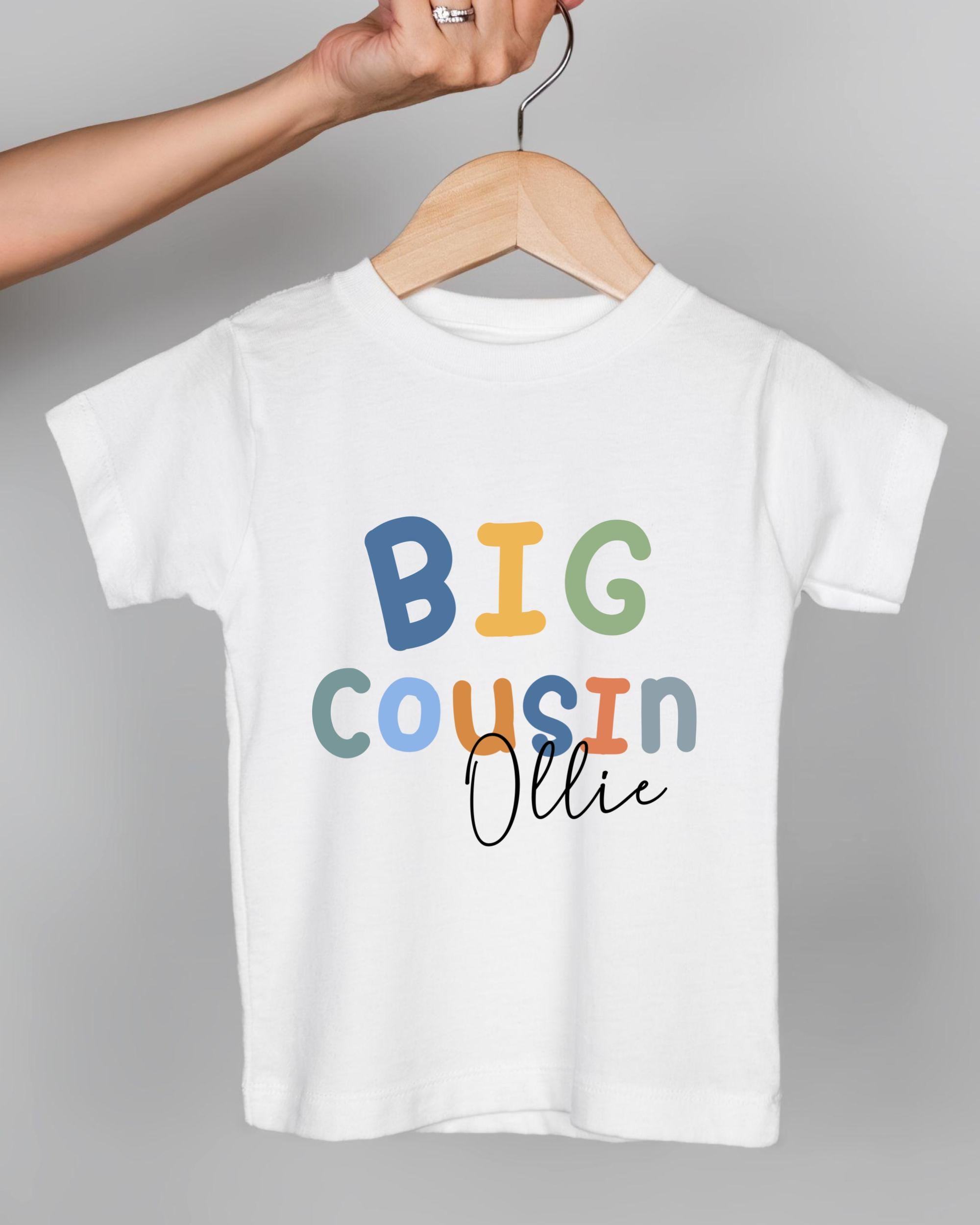 A white t-shirt with the text "BIG COUSIN OLLIE" printed on it.