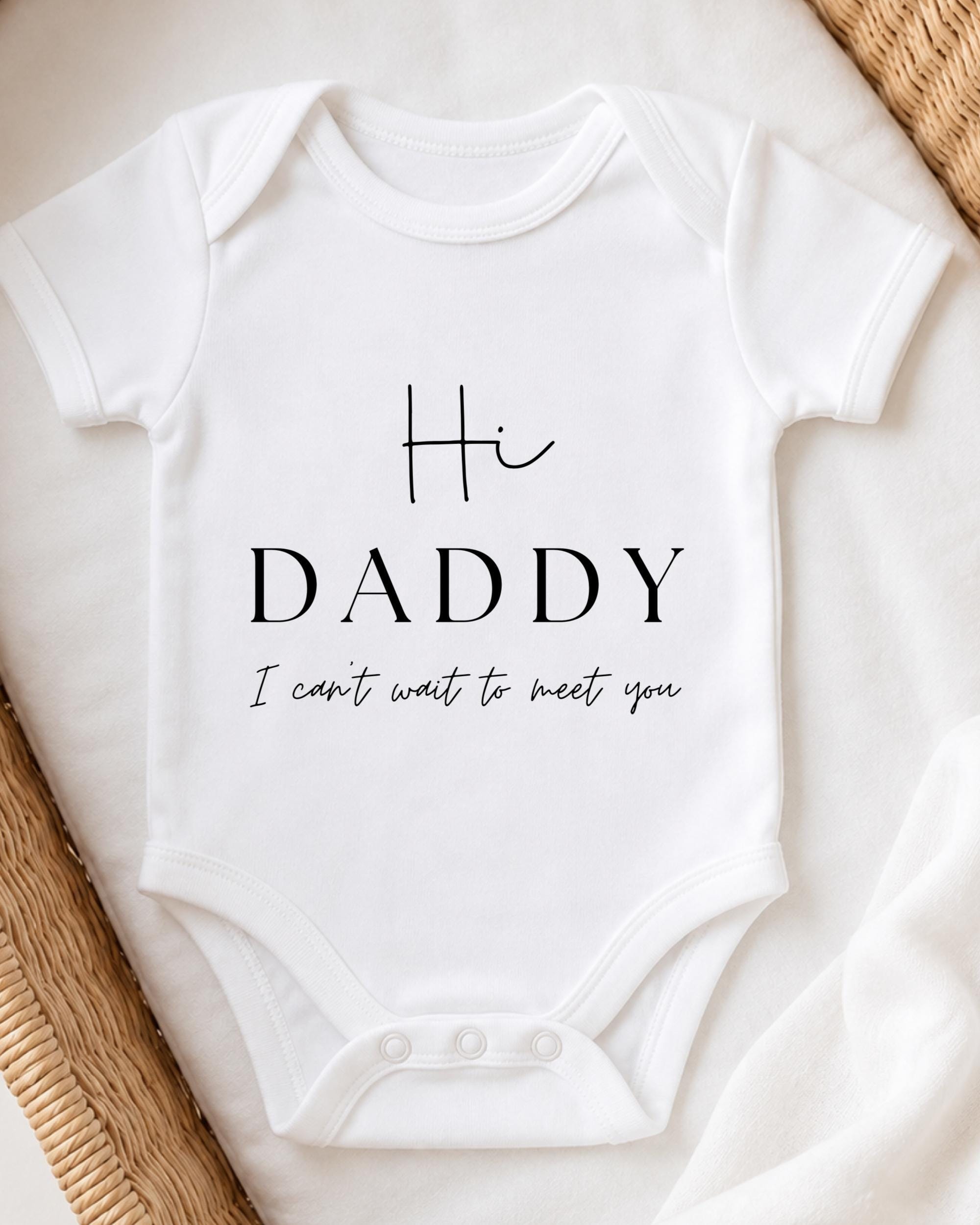 A white baby onesie with the text "Hi Daddy I can't wait to meet you" printed on it.