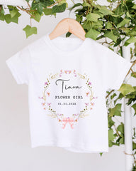A white t-shirt with a floral wreath design and text printed on it, hanging on a wooden hanger.