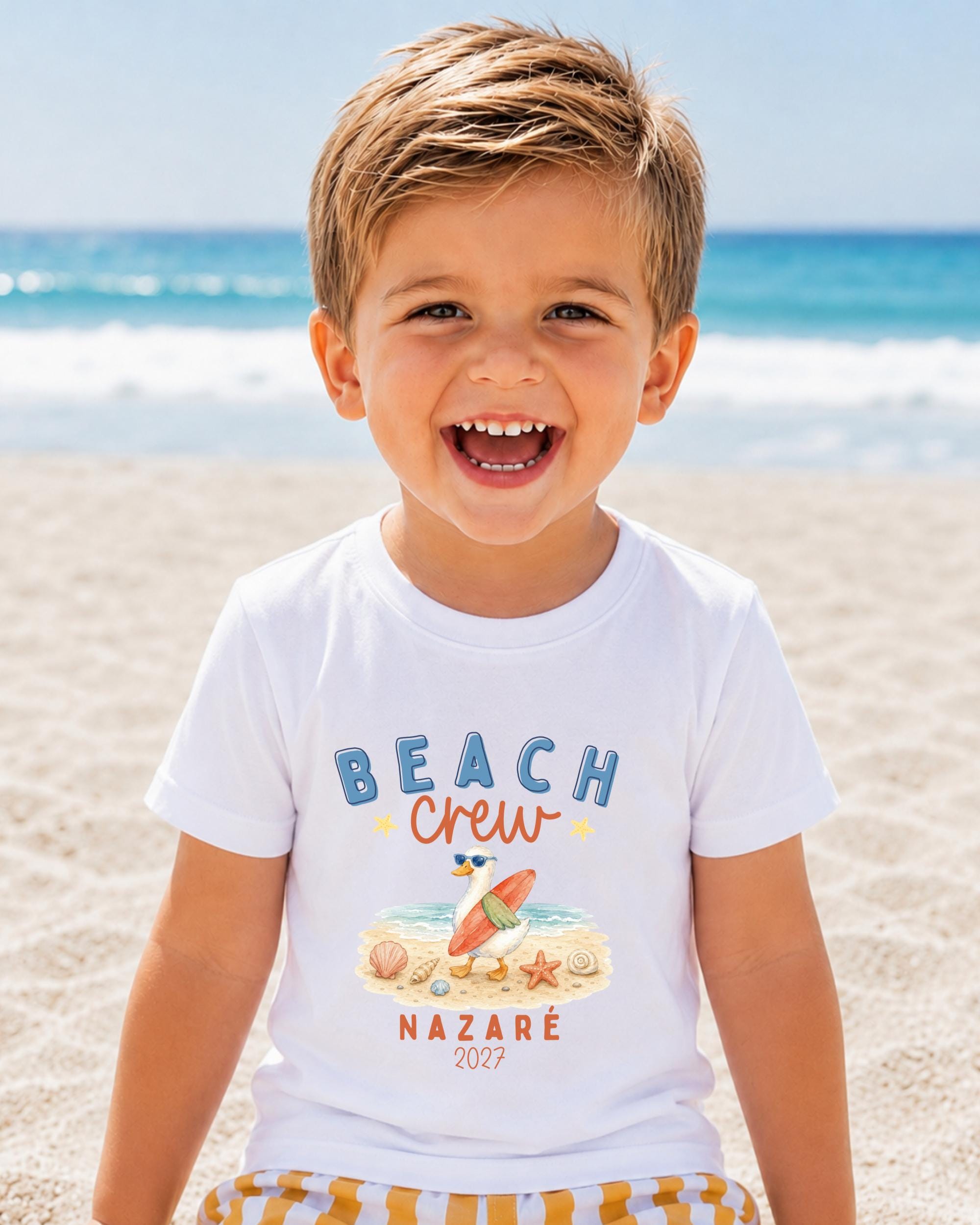 A young boy with a big smile on his face, wearing a white t-shirt with a beach-themed graphic and text.