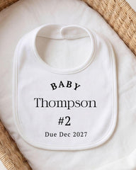 A white bib with personalized text, including the name "Baby Thompson" and the date "Due Dec 2027".