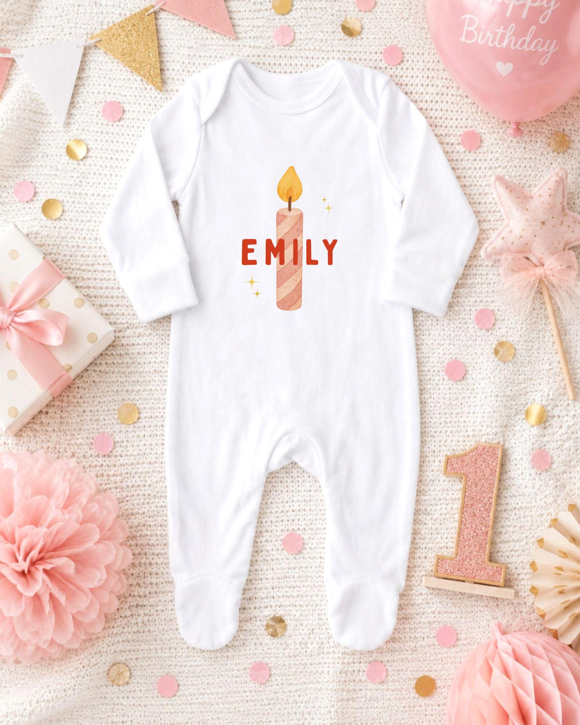 A white onesie with the name "EMILY" printed on it, surrounded by birthday decorations such as a candle, a star, and confetti.