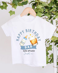 A white t-shirt with a graphic design that says "Happy Birthday Dad" and includes a bottle of milk and a glass of beer.