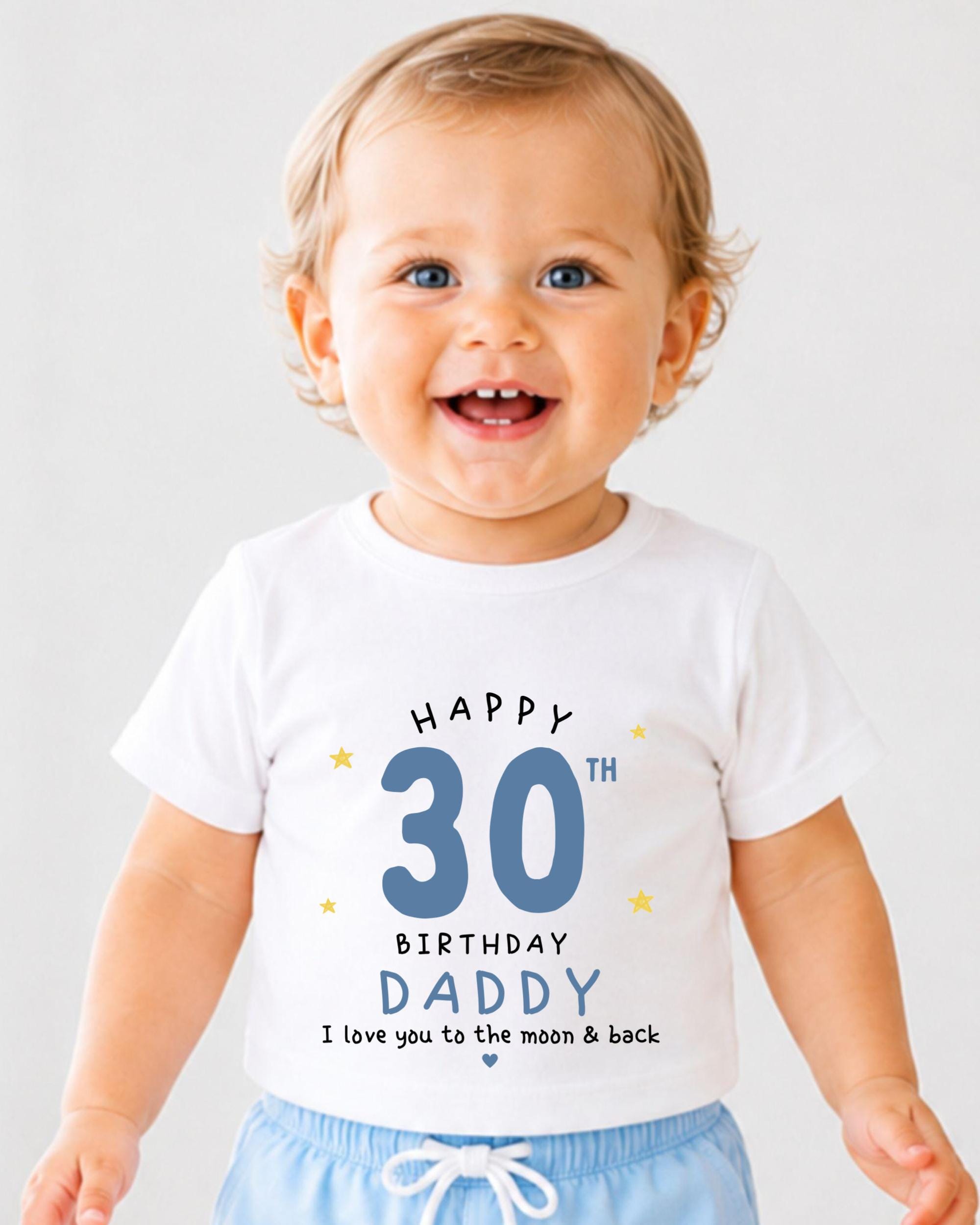 A smiling baby wearing a white t-shirt with text that reads "Happy 30th Birthday Daddy I love you to the moon & back".