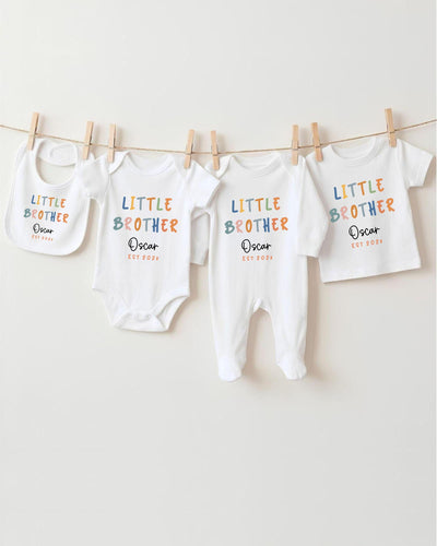 A row of four white baby clothes, including bodysuits and pajamas, hanging on a clothesline.