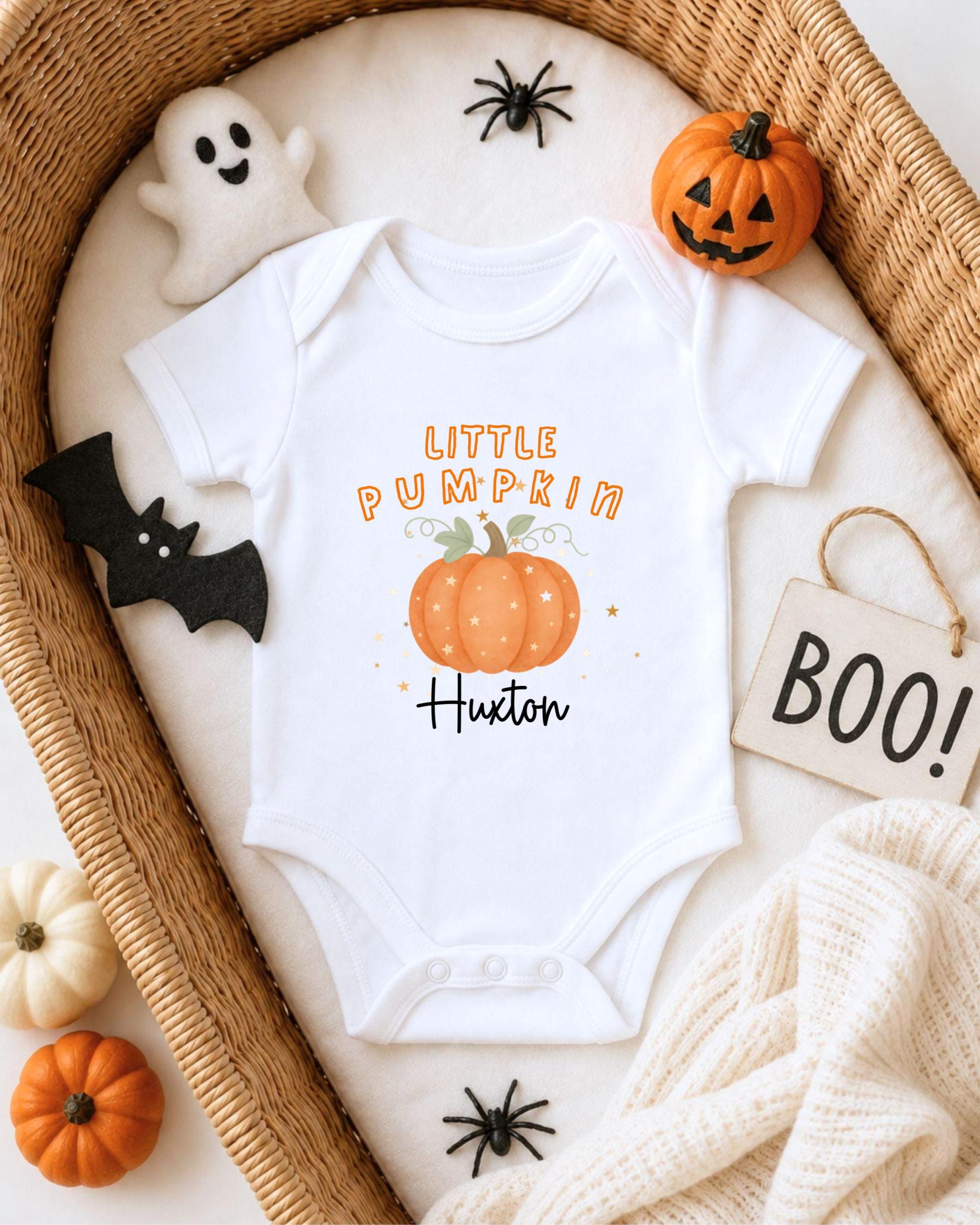 A white onesie with a pumpkin design and the text "Little Pumpkin" printed on it, surrounded by Halloween-themed items such as a ghost, a pumpkin, a bat, and a sign that says "BOO!"