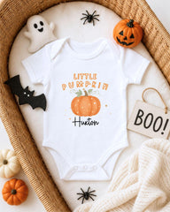 A white onesie with a pumpkin design and the text "Little Pumpkin" printed on it, surrounded by Halloween-themed items such as a ghost, a pumpkin, a bat, and a sign that says "BOO!"