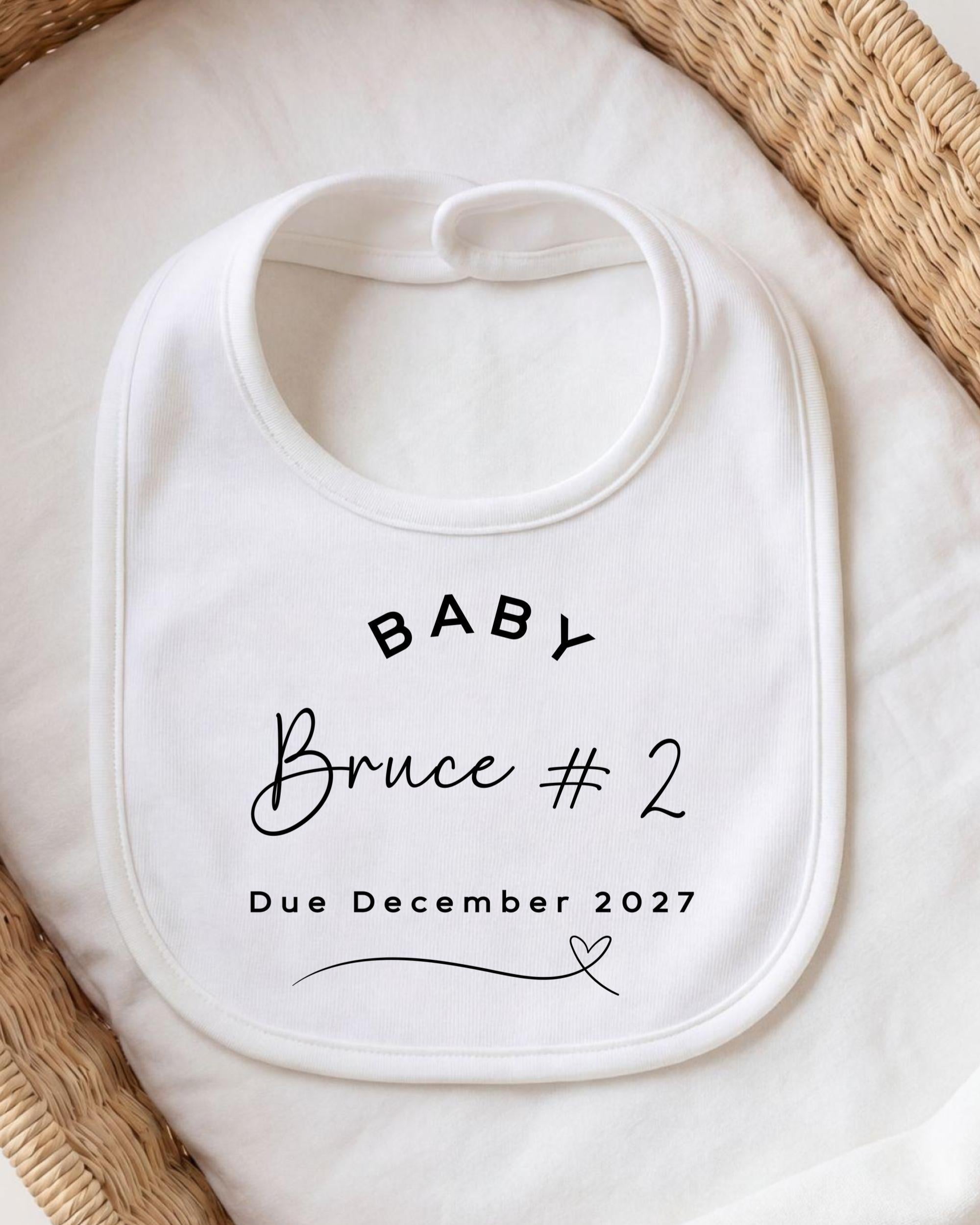 A white baby bib with text printed on it, placed on a white cloth.