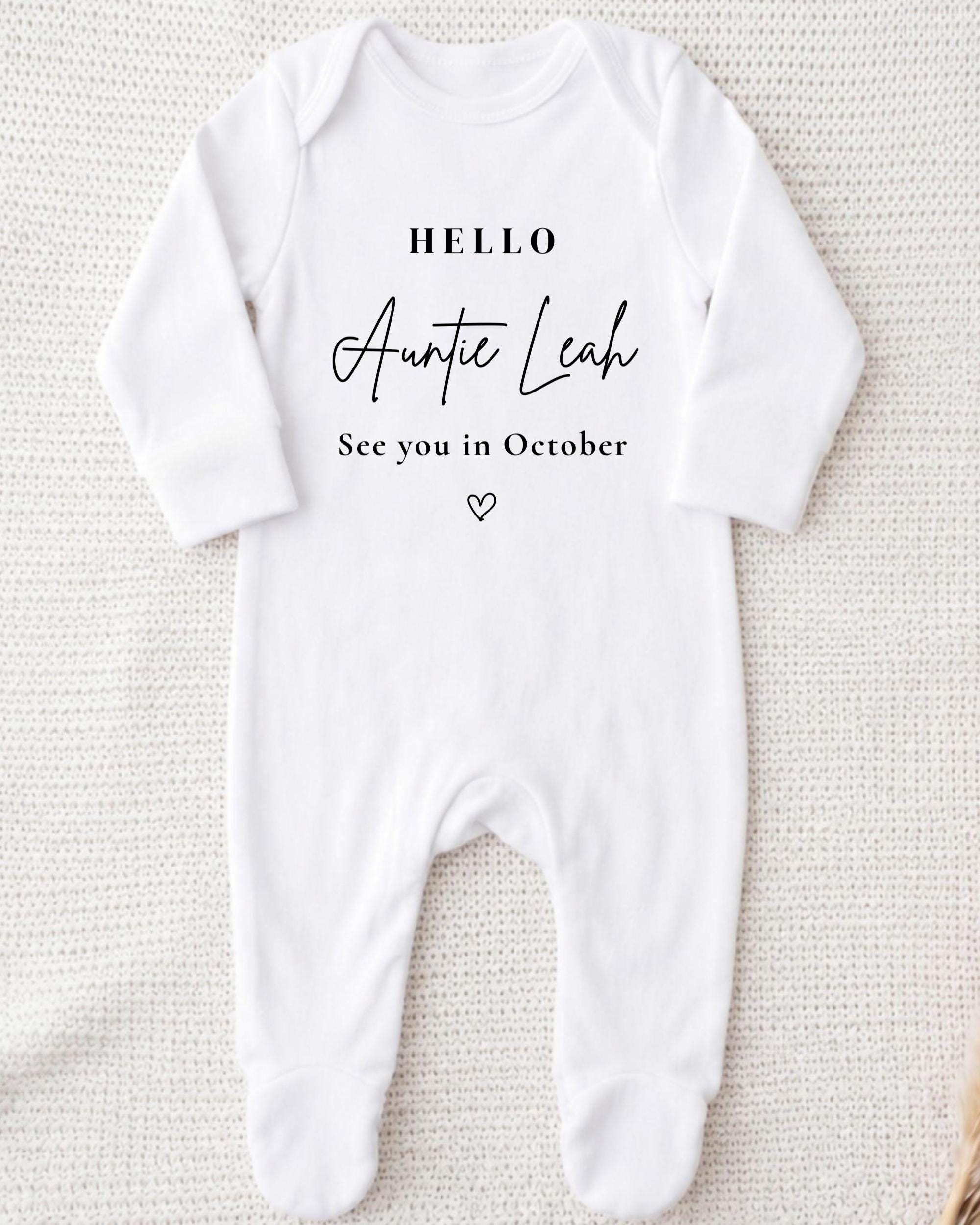 A white onesie with the text "Hello Auntie Leah See you in October" printed on it.