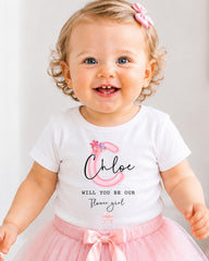 A smiling baby girl wearing a white t-shirt with a personalized monogram and a pink tutu skirt.