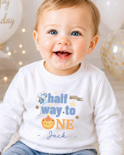 A smiling baby boy wearing a white shirt with a birthday message printed on it.