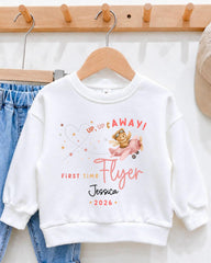 A white sweatshirt with a cartoon airplane and the text "UP, UP & AWAY! FIRST TIME FLYER Jessica *2026" printed on it.