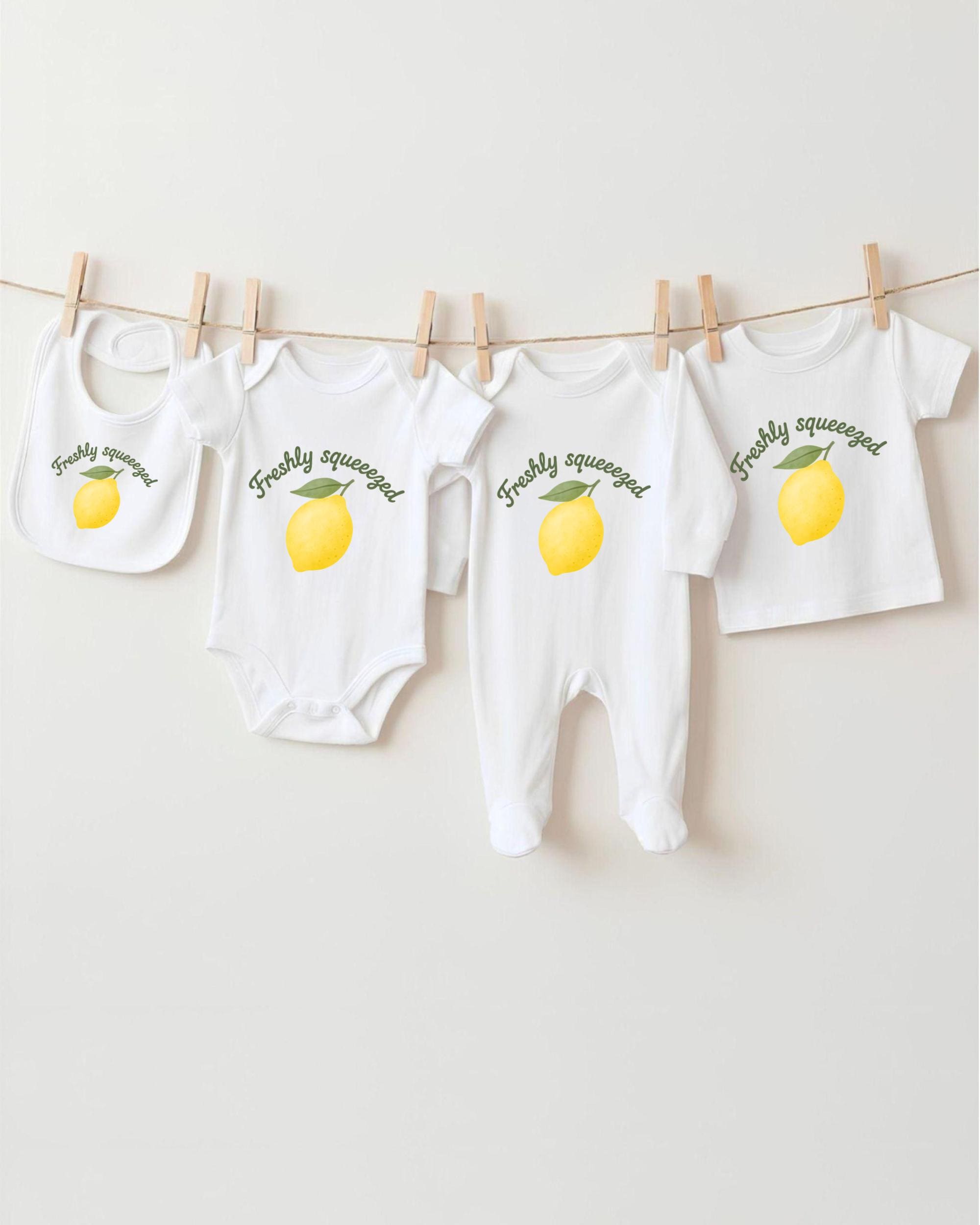 A collection of baby clothes, including onesies and bibs, hanging on a clothesline with a lemon graphic printed on them.