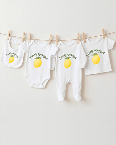A collection of baby clothes, including onesies and bibs, hanging on a clothesline with a lemon graphic printed on them.