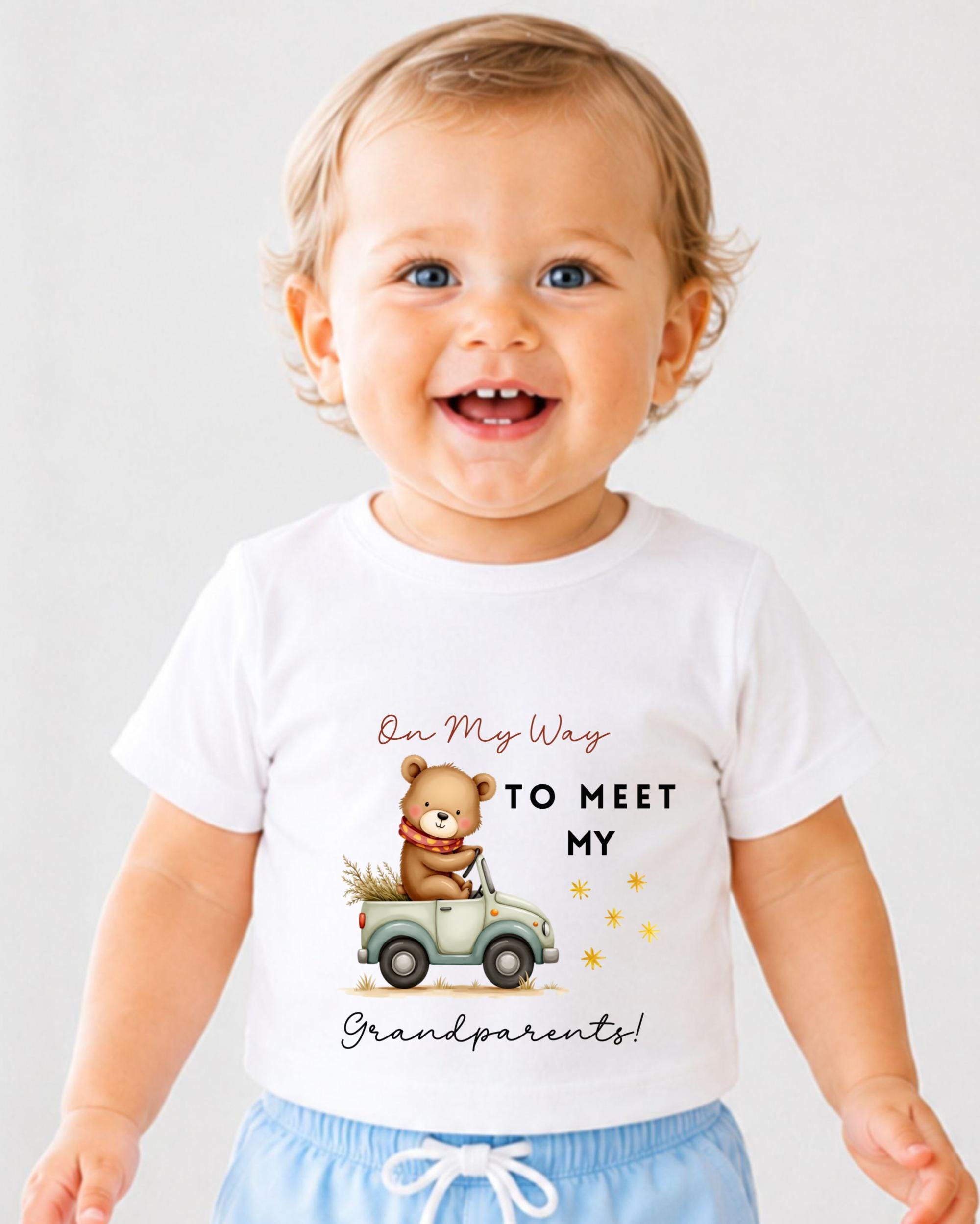 A smiling baby wearing a white t-shirt with a teddy bear and text that says "On My Way to Meet My Grandparents!"
