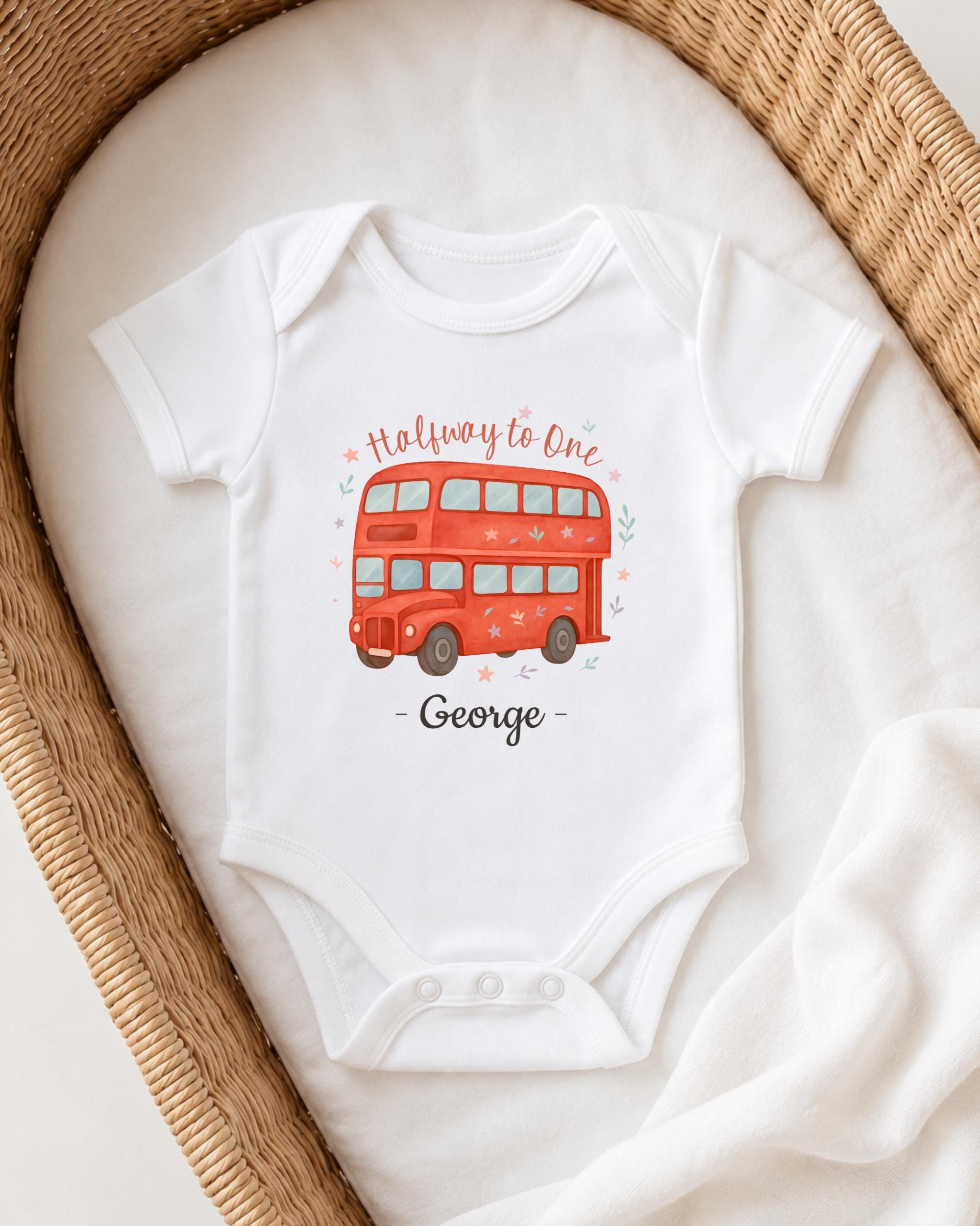 A white onesie with a red double-decker bus design printed on it, placed on a white blanket.