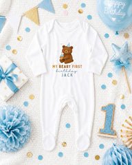 A baby onesie with a bear on it, surrounded by birthday decorations such as a blue balloon, confetti, and a star-shaped ornament.