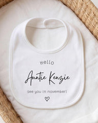 A white baby bib with a personalized message printed on it, placed on a white cloth.